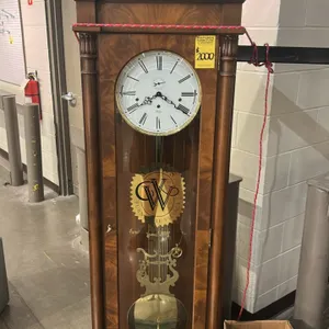 Sligh wooden regulator wall clock. Features a wood case with a glass door displaying the "Weir's Furniture Village" logo. Features a white dial with R