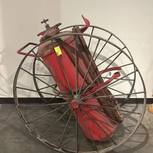 Vintage hand-drawn chemical fire extinguisher cart. Features a large red-painted steel chemical cylinder tank, dual large-diameter spoked metal wheels