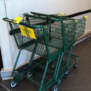 Metal shopping cart. Features a green wire basket, integrated child seat with safety strap, and a lower wire storage rack. Yellow plastic corner guard