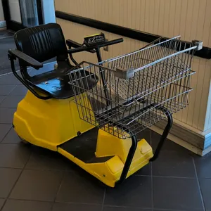 Ortho-Kinetics EZ Shopper electric shopping cart. Features a yellow molded plastic body, front-mounted wire cargo basket, and a black vinyl seat with 