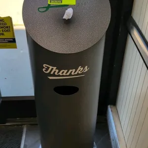 Metal sanitizer wipes dispenser. Features a textured powder-coated gray finish, top-loading wipes dispenser slot, integrated waste receptacle, and "Th