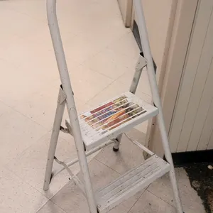 Metal 2-step folding ladder. Features a white painted frame, two ribbed steps, and a high arched handrail. Folds for storage.