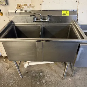 Stainless steel 2-compartment sink. Features a double-bowl design with a backsplash-mounted swing faucet and high backsplash. Supported by stainless s