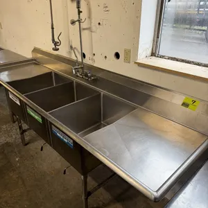 Stainless steel 3-compartment sink with left and right drainboards. Features a wall-mount pre-rinse faucet with sprayer, integrated backsplash, and th