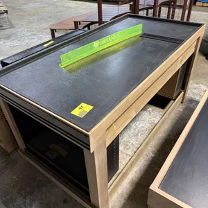 JSI Store Fixtures wooden display table merchandising island. Features a black textured top surface, integrated under-counter storage with black pegbo