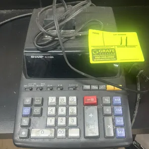 Sharp EL-2196BL 12-digit printing calculator. Features a large digit display, tax keys, and a metal paper roll holder. Equipped with an attached AC po
