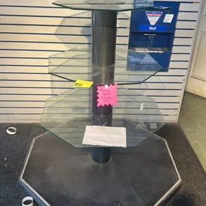 3-tier glass display merchandiser. Features three graduated octagonal glass shelves supported by a central black column. Mounted on an octagonal black