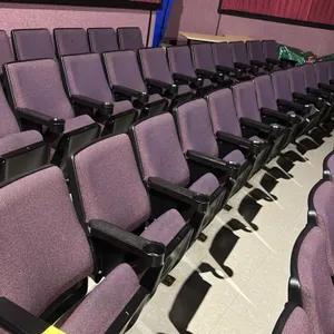 Floor-mounted movie theater seating row. Features purple cloth cushioned foldable seats, black plastic armrests with integrated cup holders, and prote
