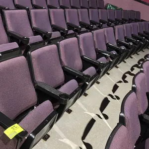 Floor-mounted movie theater seating row. Features purple cloth cushioned seats with folding/flip-up bottoms, integrated cup holders on black plastic a