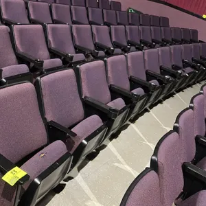 Floor-mounted movie theater seating row. Features purple cloth cushioned foldable seats and armrests with integrated cup holders. Note: Fabric on one 