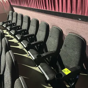 Floor-mounted movie theater seating row of (8) connected seats. Features dark gray textured cloth cushioned seats and backrests, folding seat bottoms,