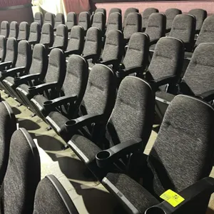 Floor-mounted movie theater seating row. Features grey and black patterned cloth cushioned foldable seats, black plastic armrests with integrated cup 