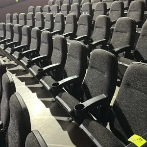 Floor-mounted movie theater seating row. Features cloth cushioned folding seats, dark textured fabric upholstery, and plastic armrests with integrated