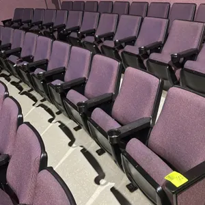 Floor-mounted movie theater seating row. Features purple cloth cushioned seats with flip-up seat bottoms, plastic armrests with integrated cup holders
