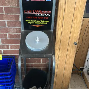 Metal shopping cart wipe dispenser stands. Features integrated sign holder frames and built-in receptacles for wipe dispenser buckets. Includes black 