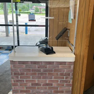 Laminate service counter. Features a light-colored laminate top, faux-brick pattern wrapped base, and a mounted clear acrylic protective sneeze guard.