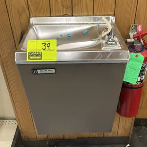 Elkay wall-mounted drinking fountain. Features a stainless steel basin with integrated drain, bubbler with guard, and push-button operation. Gray fini