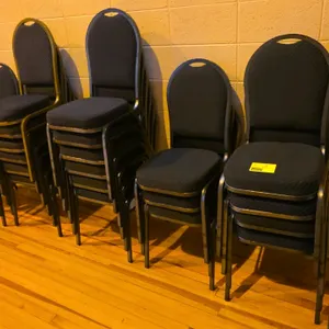 Upholstered stackable banquet chairs. Features dark blue patterned fabric cushioned seats and backs with integrated carry handles. Mounted on hammered