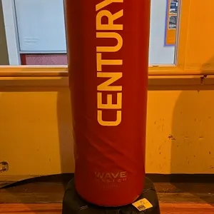 Century Wavemaster 2XL Pro freestanding training bag. Features a red vinyl cover over high-density foam padding. Mounted on a fillable black plastic b
