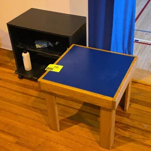 Table set. Includes one 18"H wood table with blue laminate top and one 21"H black laminate mobile side table with open shelf. Black table is mounted o