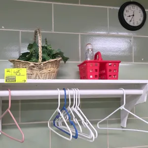 Wood wall shelf with hanging rod. Features a white painted finish. Includes contents: a wicker basket with artificial green foliage, a red plastic sho