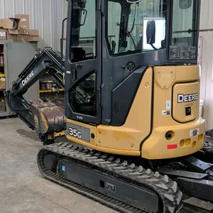 John Deere 35G mini excavator. Features enclosed cab, rubber tracks, and backfill blade. Equipped with a 24" bucket and a hydraulic thumb. Meter shows