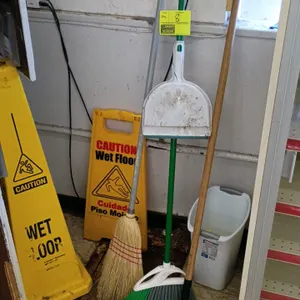 Group of janitorial cleaning supplies. Includes (1) corn broom, (1) plastic angled broom, (1) lobby dustpan, (1) wooden-handled scraper, (1) A-frame w
