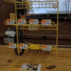 Counter top merchandiser. Features a yellow wire frame with a three-tier display configuration and integrated retail price tag ticket holders on each 
