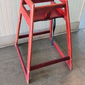 Wooden high chair. Features wood construction in a reddish-brown finish, safety restraint strap, and stackable frame design. 21" floor to seat height.