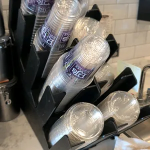 Selection of countertop cup and lid organizers. Features multi-tier angled storage compartments with a black finish. Contents not included.