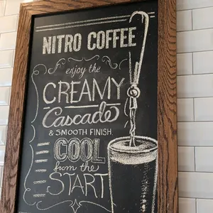 Assorted coffee shop wall signage and framed prints. Includes 36"H framed Nitro Coffee chalkboard sign, 4-section hanging wooden sign, framed drink me