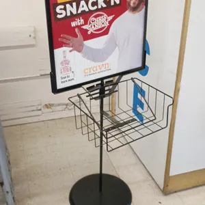 Metal sign holder. Features a top poster frame and an attached lower wire display basket. Black finish. 22" x 60". Mounted on a round base.