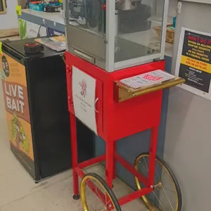 Carnival King popcorn machine on cart. Features popping kettle, light and pop switches, side utility shelf, handle, and storage base. 26"W x 15"D x 57