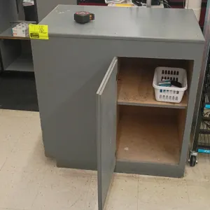 Wood checkout cabinet. Features gray laminate exterior, integrated multi-slot cash or ticket drop insert, open cubby, lower compartment, and rear hing