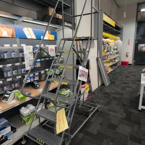 Rolling metal stock ladder. Features 7-step construction with perforated slip-resistant treads, tubular steel frame, dual side handrails, and upper gu