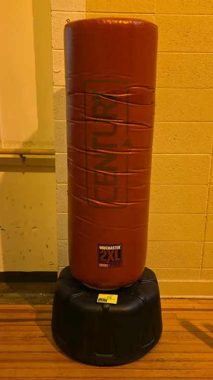 Century Wavemaster 2XL Pro freestanding training bag. Features a high-density foam-filled striking surface with a red vinyl cover. Mounted on a low-pr
