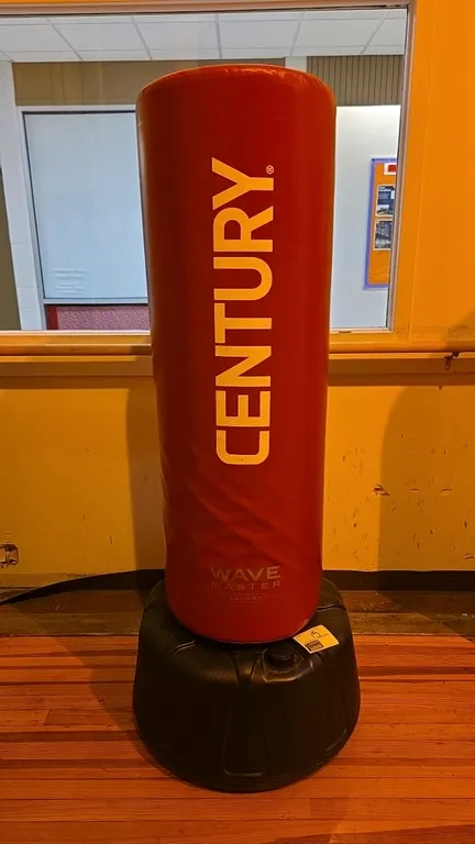 Century Wavemaster 2XL Pro freestanding training bag. Features a red vinyl cover over high-density foam padding. Mounted on a fillable black plastic b