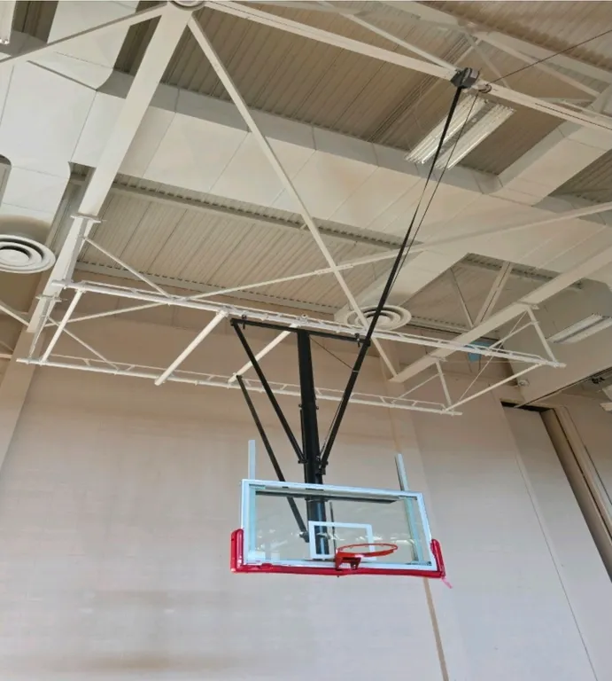 Porter Athletic ceiling-mounted basketball hoop. Features a 10' regulation height glass backboard with red bottom padding, orange breakaway rim, and n