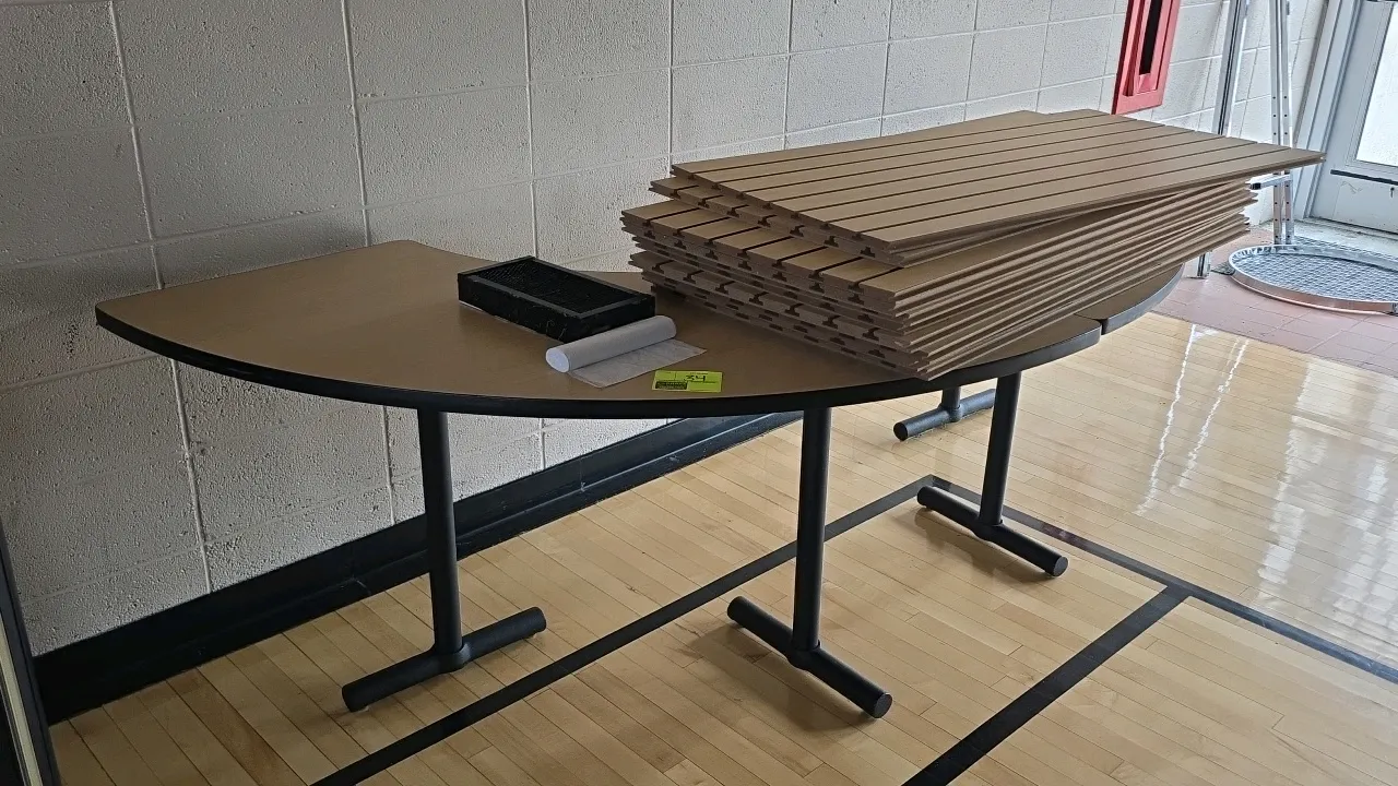 Laminate wood table. Features a curved light wood-grain laminate top with black trim. Mounted on a black metal base. Dimensions: 99" x 30"H. Note: Sla