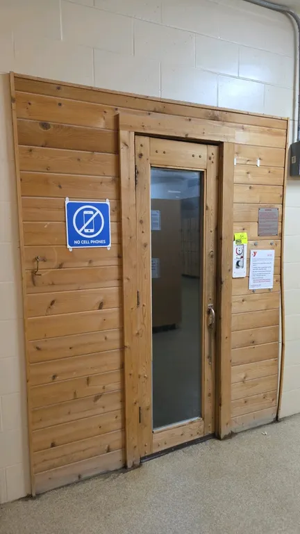 Finlandia sauna room. Features wood panel construction, a wood door with a full-length glass pane, and multi-tier interior bench seating. Equipped wit