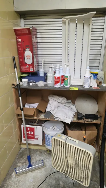 Wooden utility shelving unit with contents. Includes a 3-speed box fan, an Ace deck and bleach sprayer in box, cleaning chemical spray bottles, bucket