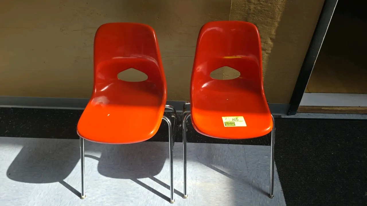 Fiberglass chairs. Features orange molded fiberglass shells with integrated lower backrest handle cutouts. Mounted on chrome-plated tubular metal fram