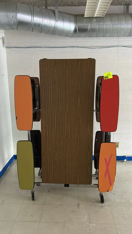 Foldable mobile cafeteria table. Features a faux-woodgrain laminate tabletop and integrated multi-colored bench seats in orange, red, and green. Foldi