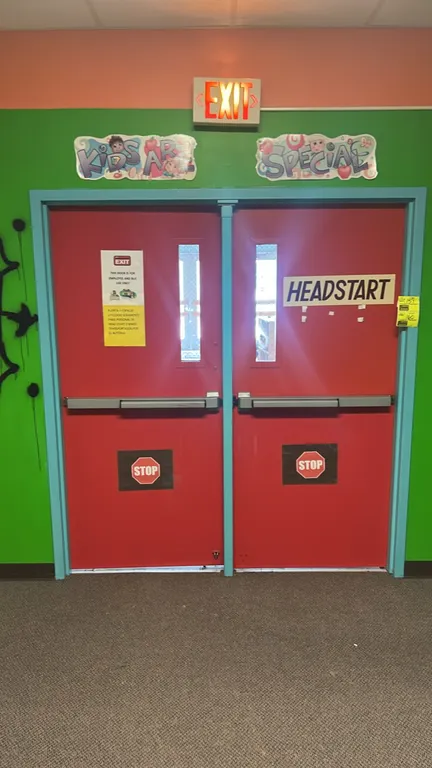 Commercial metal and wood double doors with frame. Features red painted finishes, narrow vertical wire-glass vision lites, and push-bar exit panic har