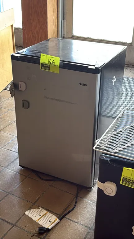 Haier compact refrigerator. Features a silver-finished door, black cabinet, interior wire shelf, upper chiller compartment, and in-door bottle storage