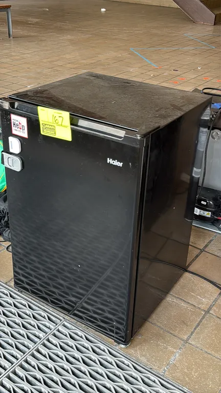 Haier compact dorm refrigerator. Features a black finish, integrated top-freezer compartment, a single wire shelf, and built-in door storage with beve