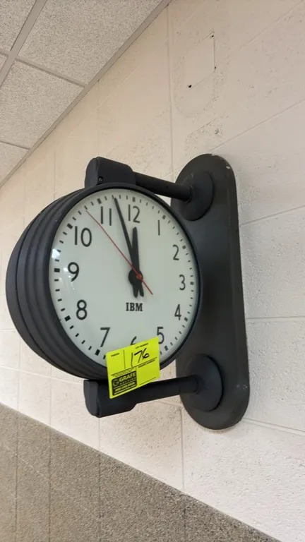 IBM 12" double-sided metal hallway clock. Features dual white analog dial faces with block IBM logos, black Arabic numerals, black hour and minute han