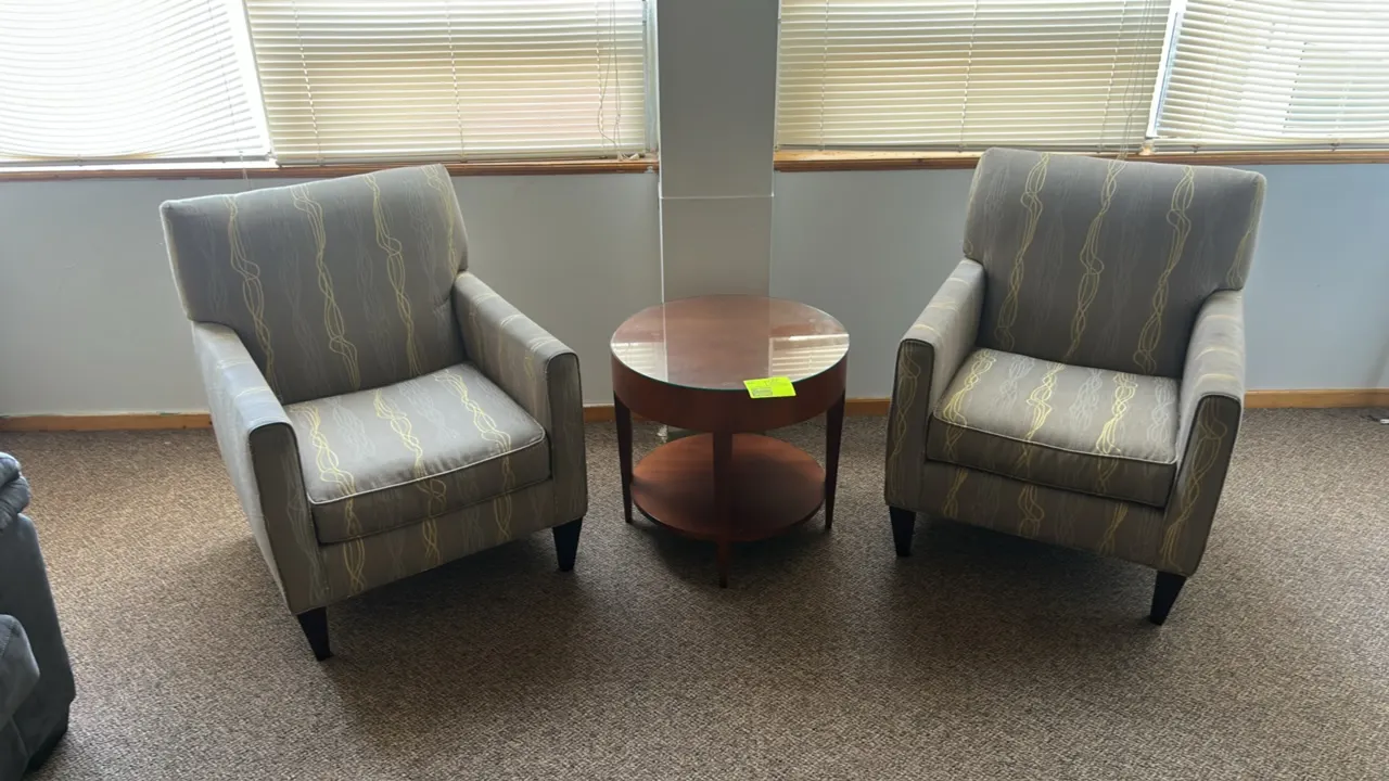 Lounge furniture set. Includes a 2' wooden round accent table with a glass top and lower shelf, and two cushioned armchairs. The armchairs feature pat