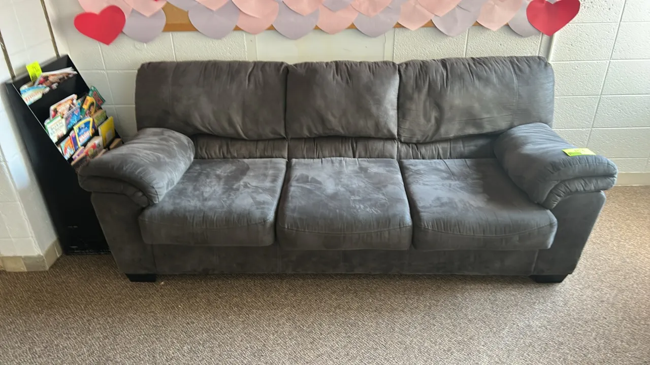 Cushioned sofa. Features plush gray microfiber upholstery, a three-seat design, and rolled cushioned armrests. Supported by block feet. 7'L. Backgroun