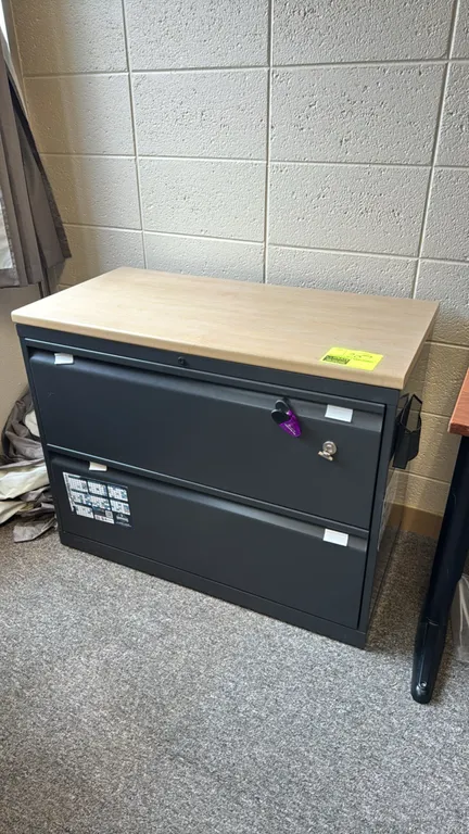 Metal 2-drawer lateral file cabinet. Features a light woodgrain laminate top and a lock with included key. Top drawer includes a plastic utility organ